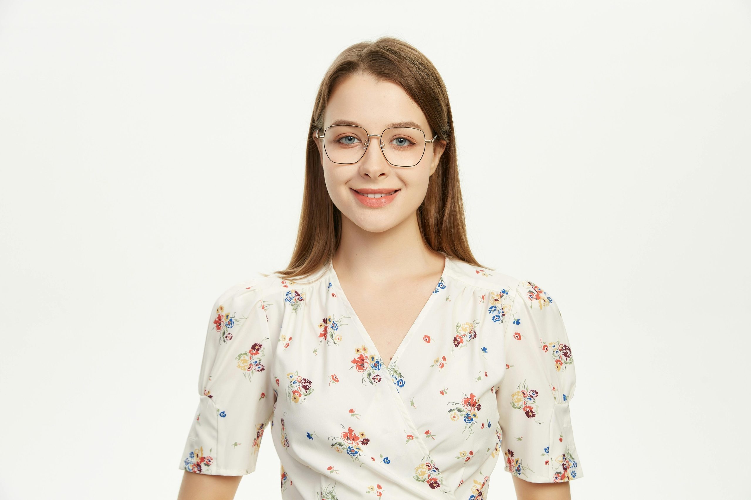 Young woman wearing glasses smiling in a floral outfit against a plain background.
