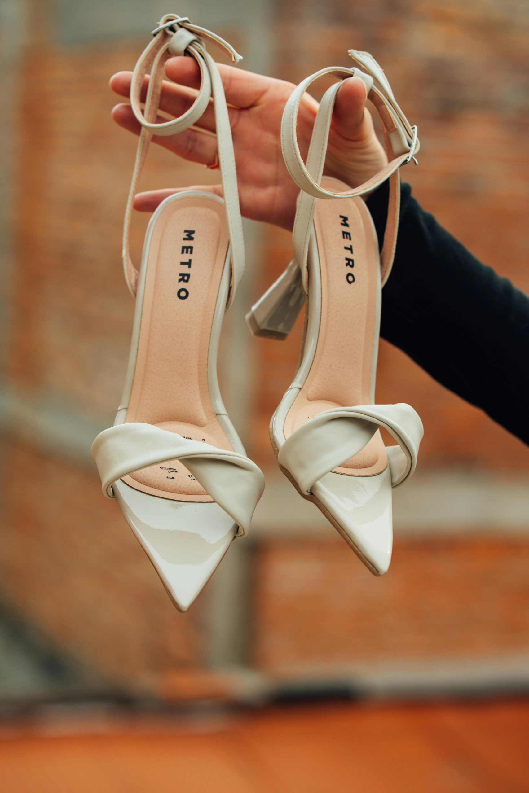 Chic beige high heels with a pointed toe design held outdoors by hand.