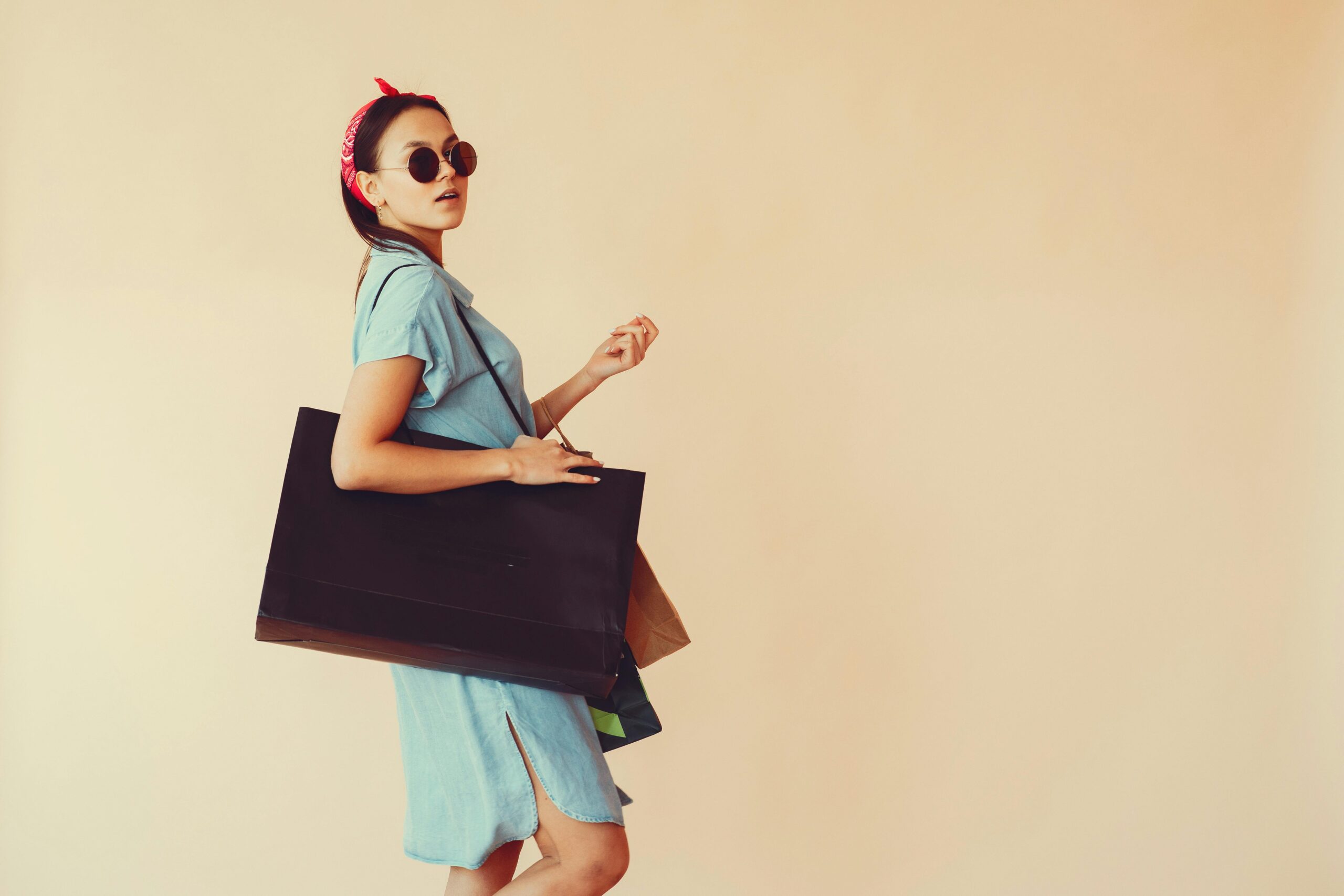 Fashionable woman in blue dress carrying shopping bags, exuding elegance and modern style against a beige background.