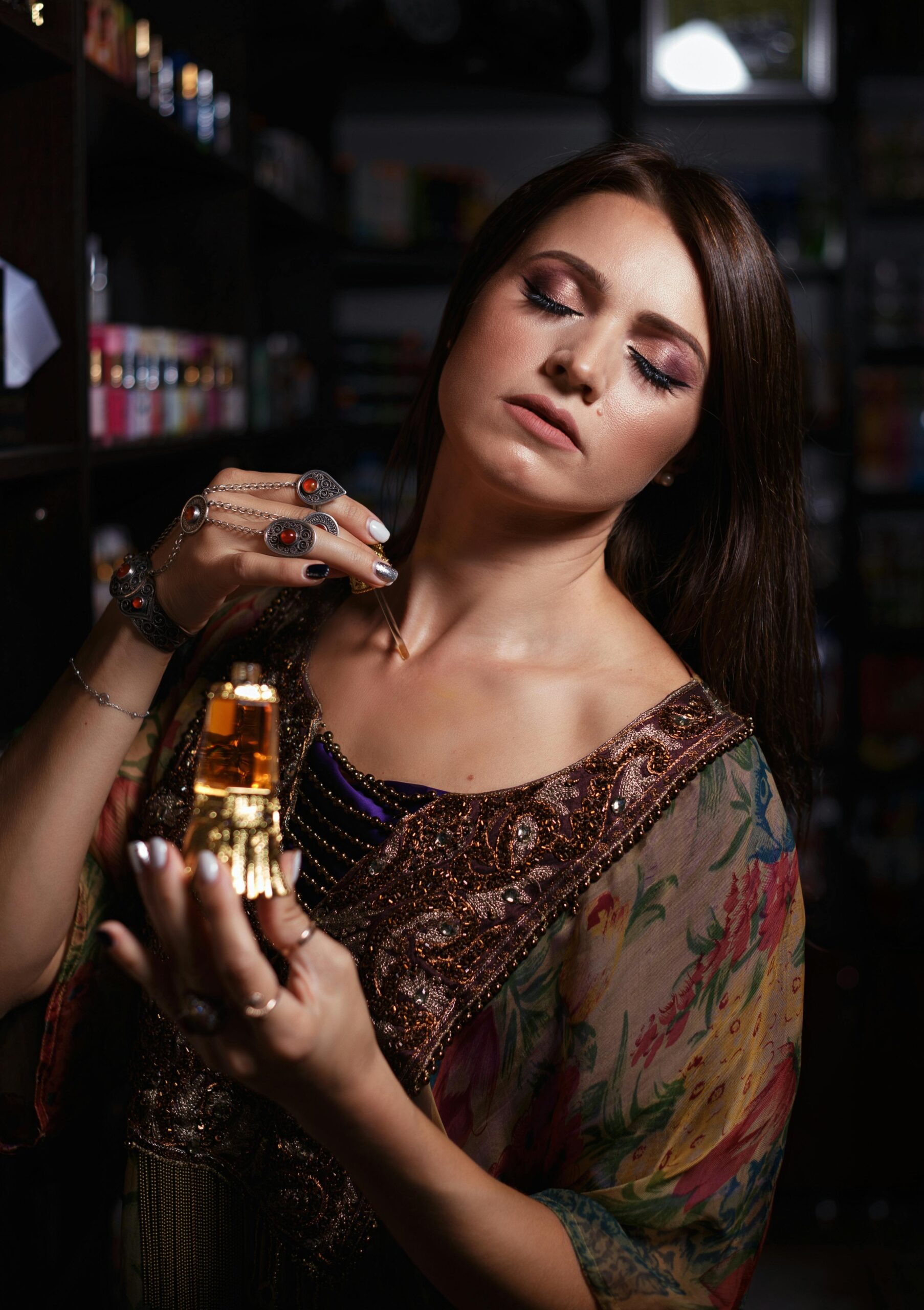 A woman in an elegant gown applies perfume, embodying grace and charm in a dimly lit setting.
